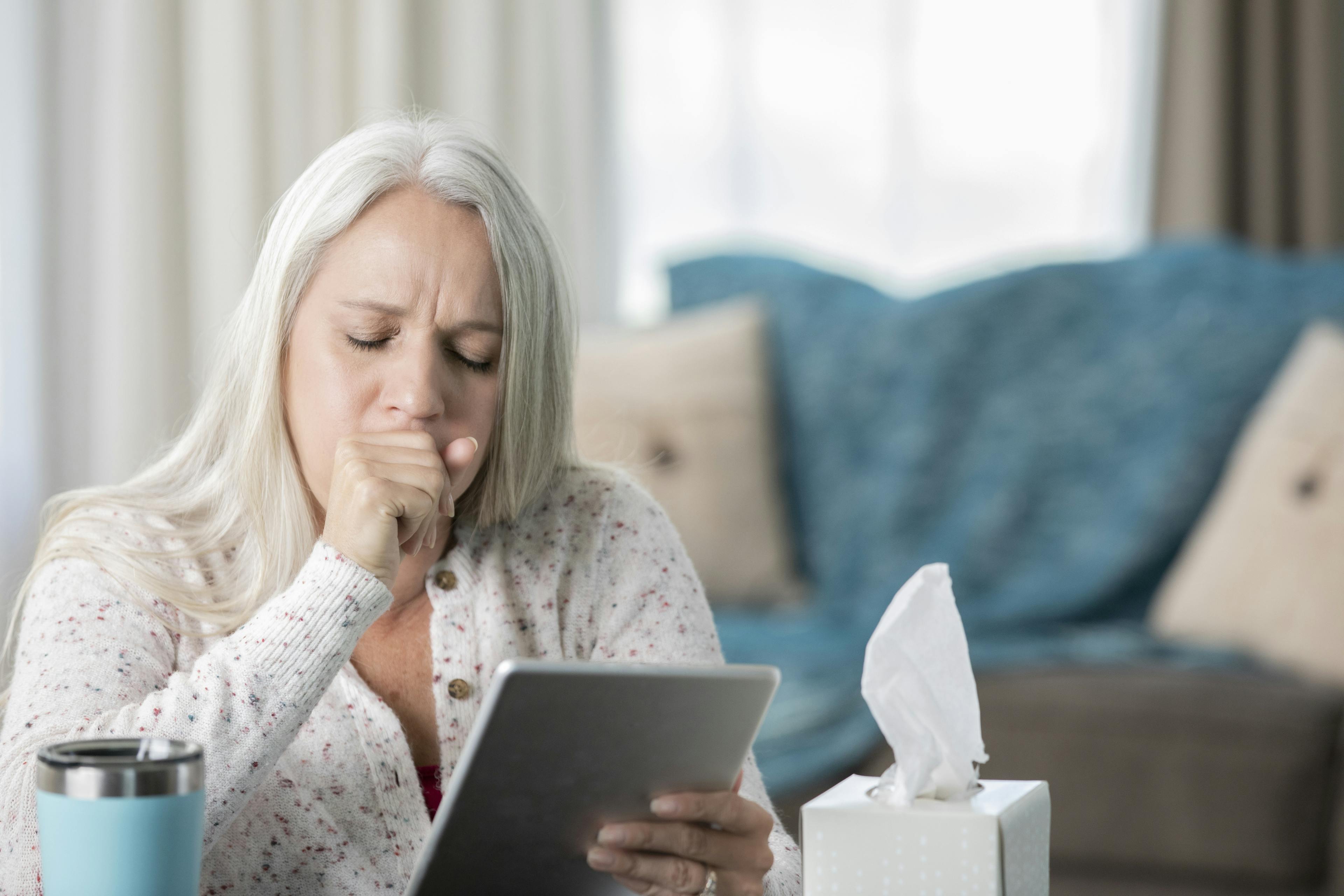 Senior woman coughs while having telehealth appointment on digital tablet with her doctor